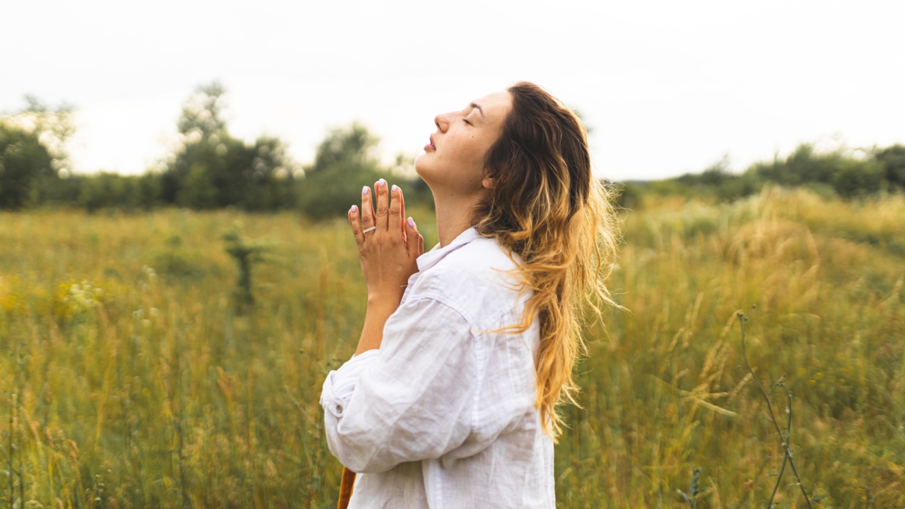 Frau mit gefalteten Händen und geschlossenen Augen auf einer Wiese