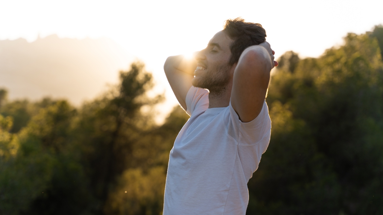 Man mit verstränkten Armen hinter dem Kopf vor Waldhintergrund