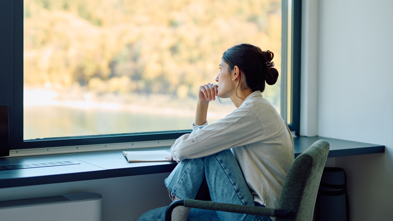 Frau mit angezogenen Beinen vor einem Fenster