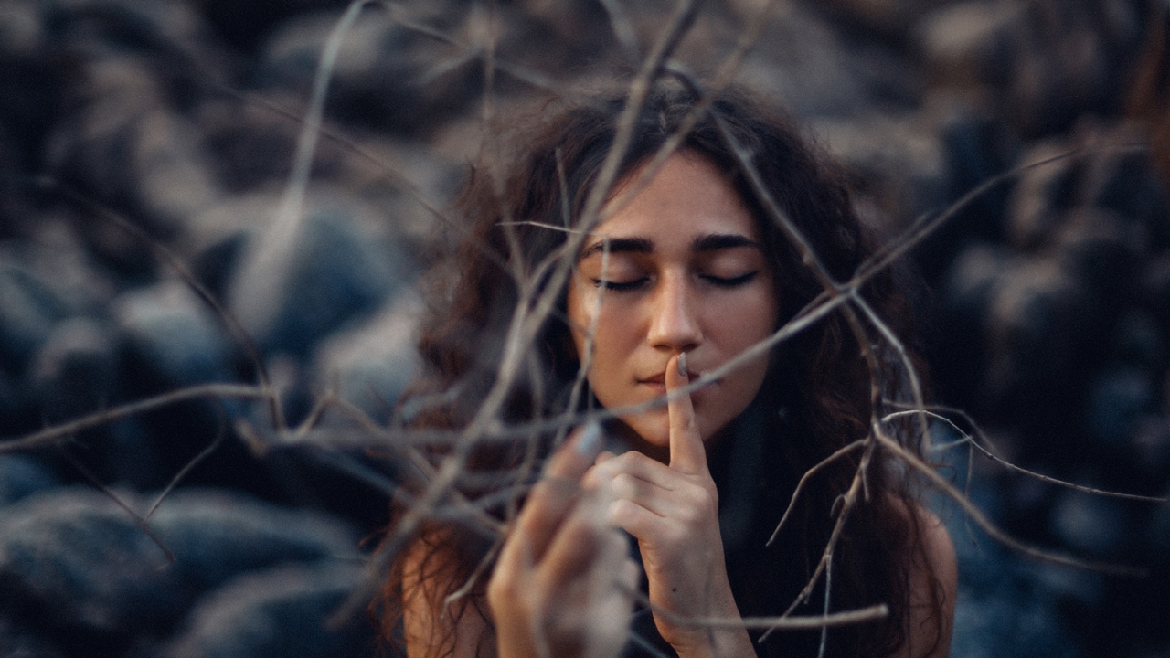 Frau mit Zeigefinger auf den Lippen und geschlossenen Augen