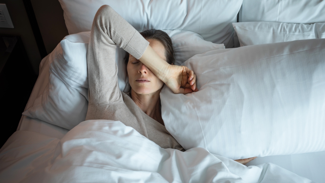 Frau liegt im Bett mit Arm über dem Gesicht