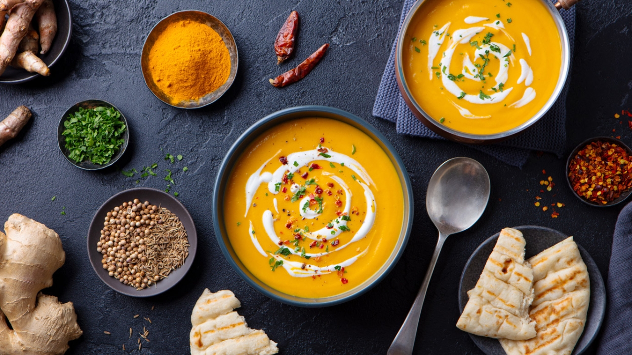 Schwarze Platte mit orangener Crèmesuppe und Gewürzschalen