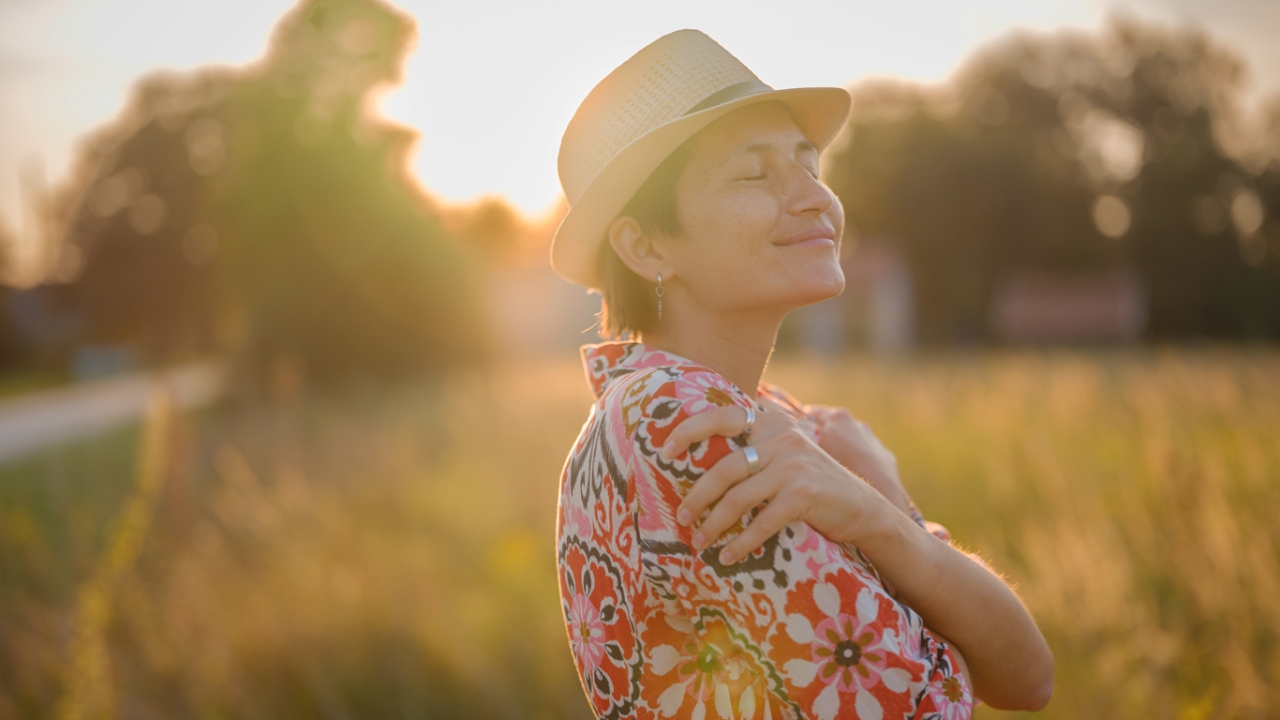 Frau die sich selbst umarmt vor Wiesenhintergrund
