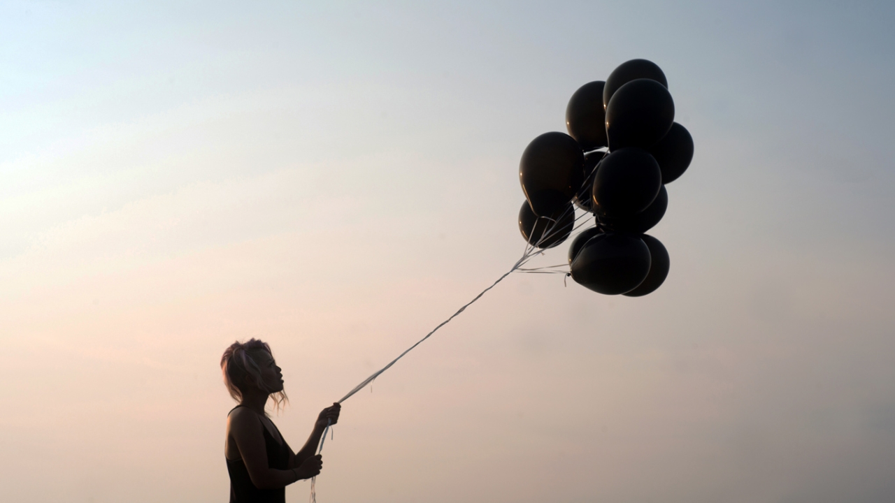 Seitenprofil einer Frau mit Luftballons in der Hand vor rosafarbenem Himmel