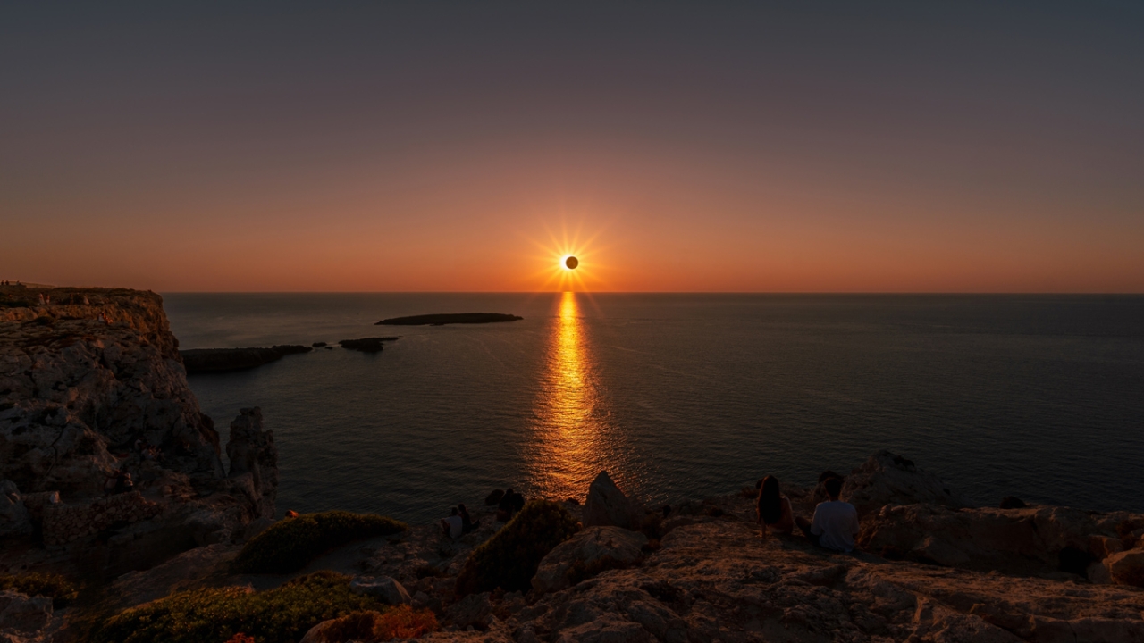 Sonnenuntergang im Zentrum des Horizontes mit schwarzem Kreis vor der Sonne vor einer Wasseroberfläche